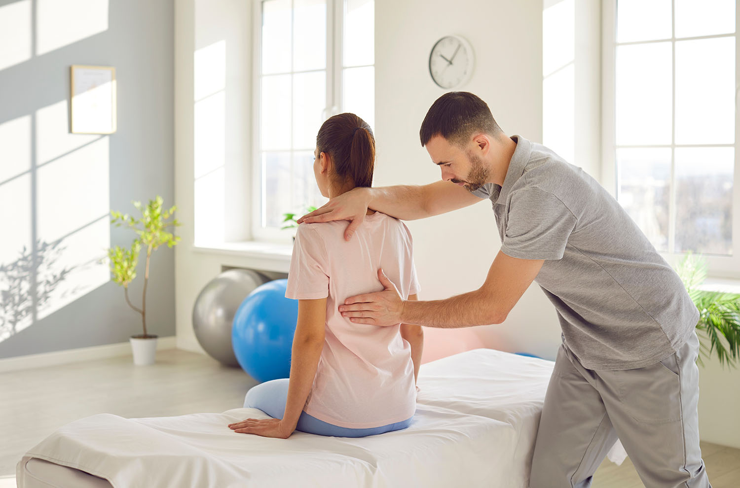 Male osteopath examining young woman in modern office. Young physiotherapist doing healing treatment on woman back in rehabilitation clinic. Chiropractor helping patient with scoliosis and back pain