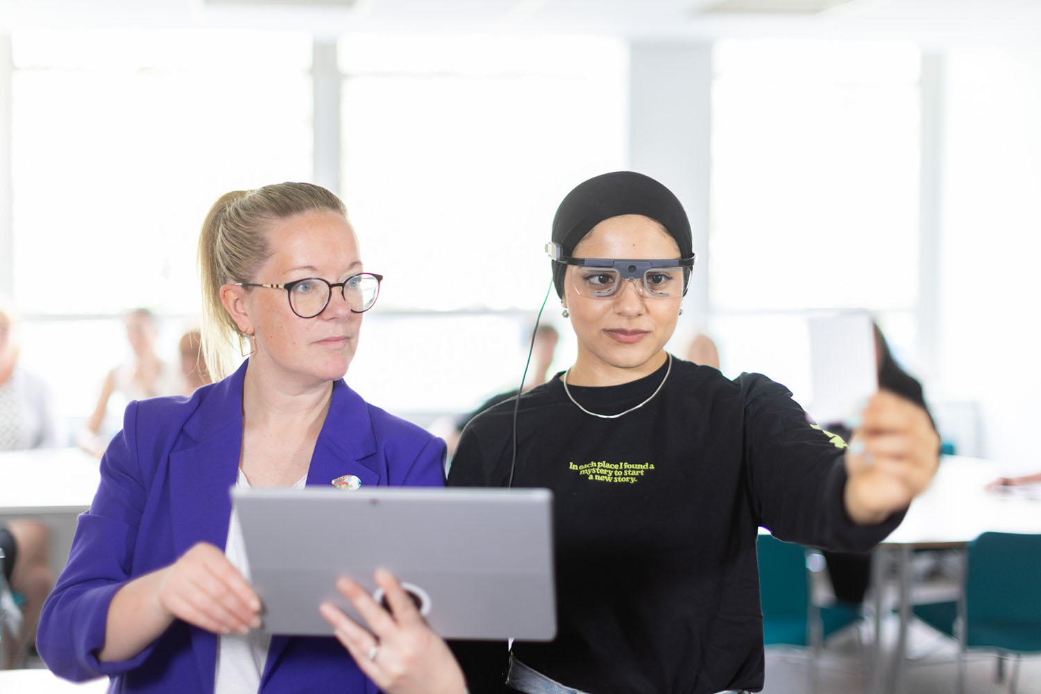 One woman is demonstrating something to another, holding a laptop.